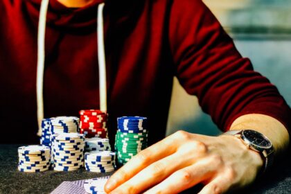 person holding playing cards beside poker chips